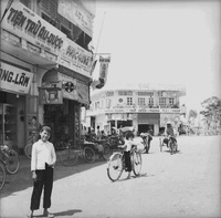 "Ca Mau" Young Vietnamese girl poses for the camera on a street as others pass her by on their bikes in the street.
