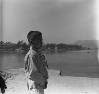 "Macau" A young boy stands the shore and looks out along the water.
