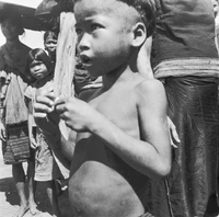 "Montagnards - Showplace Strat. Ham - 8-21-62 - In MTs - Faces - Blockhouses" A young boy is looking away from the camera with other villagers surrounding him.