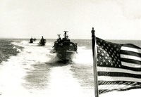"SWIFTS boats try-out their sea legs upon arrival in Vietnam. Six SWIFTs arrived on Christmas Eve to join two others in Operation Market Time patrols off Phu Quoc Island in the Gulf of Thailand. Manned by U.S. Navy crews, these boats will patrol in conjunction with other Market Time unit to prevent infiltrations of men, arms and equipment by the Viet Cong." A line of five boats in open water. An American flag is in the lower right corner of the frame.