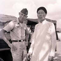 An American soldier is posing next to a villager for a photo. There is a Jeep in the background.