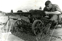 "Tuy Hoa, Vietnam - Specialist Four John Crews, of 1st Brigade , 101st Airborne Division paratrooper sits behind an enemy 12.7mm heavy machinegun captured by the 2nd Battalion, 502nd (Airborne) Infantry during an engagement with the 95th North Vietnamese Army Regiment near Tuy Hoa on Operation Geronimo I. Seventy-three enemy were killed and 44 captured in the battle while friendly causalities were light." An American soldier aims a machine gun mounted on wheels. He sits on a tarp in the grass.