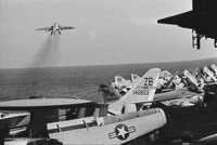 "7th Fleet" A row of Navy airplanes sitting on an aircraft carrier in open water. One airplane has just taken off.