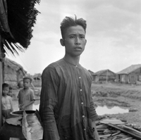 Original title: "VN Life", a potrait of a Vietnamese man standing on a dirt village road. There are two children in the background.