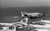 Five Naval planes sitting on an aircraft carrier in open water.