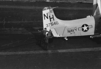 "7th Fleet" A Naval plane on an aircraft carrier. Two American men in uniform adjust a flap near the tail of the plane.