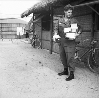 An American woman is holding several boxes as she looks down at them, bicycles line a building wall in the background.