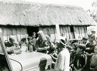 An American soldier treats a young child's eye with some medical supplies. There is a crowd of children around them.