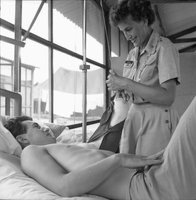 An American nurse is smiling at her patient as she adjusts the position of his arm.