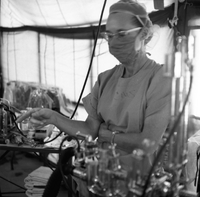 A nurse in surgery scrubs points to something in an operating room.