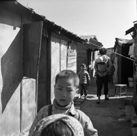 "Macau" A slum street scene.  A young boy is in the foreground wih others walking away from camera in the background.