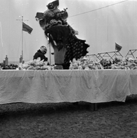 Original title: "VN Life" The photo probably shows celebrations for Tết Trung Thu. There is a large table in the foreground with small plastic bags on it (possibly containing candy or some other fetival favor). There is a lion dance being performed in tha background and a child in a mask dancing. There are children watching the dance, and some star-shaped lanterns in the far right of the frame. Several South Vietnamese flags fly in the background.