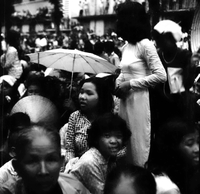 Women standing in the crowd- one is holding an umbrella. (Dark Photo)