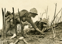 Two American soldiers are seen in what appears to be a trench. One is holding a walkie and the other is holding a gun.