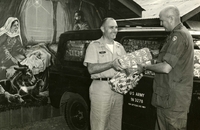"Saigon - Stacking gifts from Texas literally to the roof of their vehicle, Army Chaplains (Capt.) Fred Hanley (Boston, Mass.) and (Lt. Col.) Edwin F. Hall, Jr. (Pomona, Calif.) prepare to distribute them to patients in U.S. Army hospitals facilities in Saigon area. The presents were contributed and sent to the 1st Logistical Command in Vietnam by the Plymouth Park Baptist Church in Irving, Tex. Priority in the distribution was given to patients admitted so recently their mail from home had not 'caught up.'" Two American soldiers stand in front of an Army Jeep filled with Christmas gifts. One soldier hands gifts to the other and smiles. A mural of Jesus in the manger is on a wall in the background.