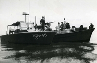 "Harbor Defense - The crew of a U.S. Navy Harbor Defense craft in Cam Ranh Bay, Vietnam, search a passenger junk, checking personal identification and looking for equipment which could be used to sabotage the cargo ships at anchor there. The LCPLs, a unit of the Harbor Defense Force of Operation Stable Door, patrol the sheltered harbors of Vietnam to ward off threats to ships bringing vital supplies to Free World Forces. Operation Stable Door is part of the Coastal Surveillance Force which also conducts Operation Market Time." Two small motor boats on the open water. There are American soldiers and Vietnamese people onboard.