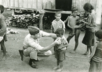 An American soldier helping a child by blowing his nose. Other children are watching around them.