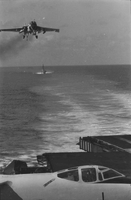 "7th Fleet" A view of the open ocean. A low-flying airplane approaches the aircaft carrier from which the photo was taken. In the background a second aircraft carrier can be seen.