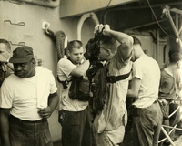 "Fighting the Fire on USS Oriskany - an Oriskany officer puts on his oxygen breathing apparatus in preparation to fight the major fire on the aircraft carrier for three hours." A group of American men stand together, possibly on the deck of a ship.  One man in the center puts on a gas mask.