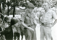 Two soldiers are speaking with villagers. One named Hibbs is looking at his hand.