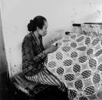 "Indonesian Arts and Crafts Negs [Negatives]." A Indonesian woman applies wax to a piece of fabric to create batik. She holds a canting in one hand and the fabric in the other. From a scrapbook page 10.