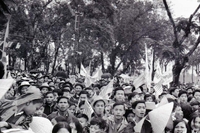 A crowd of Vietnamese people holding flags and banners. They have both American and South Vietnamese flags.