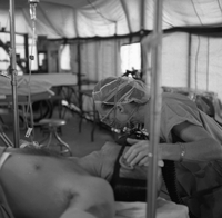 A nurse listens to a patients breathing as she leans over his head.