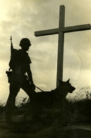 Silhouette of an American soldier and his dog standing in front of a large cross.