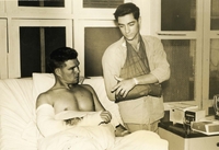 "Saigon, Vietnam - Twenty-four hours after both men received wounds from the same bullet, Army 2nd Lt. Johnny L. Bryant (Maryville, Tenn.) left, and Warrant Officer Bruce L. Carter (Leeds, Utah) exchange recollections in Saigon's Third Field Hospital on how they landed their chopper safely despite being disabled. The pair are Army aviators with the 13th Combat Aviation Battalion's 114th Assault Helicopter Company." Two American soldiers in a hospital with their arms bandaged. One is in a hospital bed and the other stands next to him.