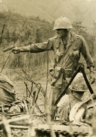 American soldier is seen pointing his gun to something out of the shot. A soldier is seen looking in the foreground.