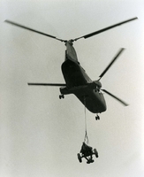 "Up and Away - A U.S. Marine assault transport helicopter from the assault ship to USS Princeton lifts artillery to the beach during the vertical envelopment phase of Operation Recon Star, 21 miles southeast of the demilitarized zone." A helicopter flies above the camera carrying something tied to a rope. It appears to be some sort of vehicle with wheels.