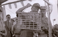 Nguyá»…n KhÃ¡nh appears to be holding some kind of animal in a small cage, possibly a monkey. Others look on the background.