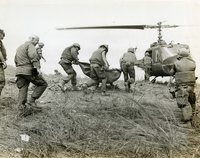 Several American soldiers are carrying someone in a cloth stretcher up towards an awaiting helicopter.