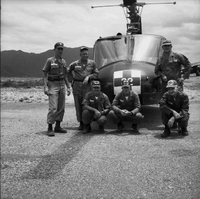 A group of American soldiers pose for a photo in front of a helicopter.  One holds a monkey.