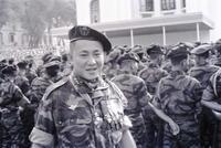 A Vietnamese soldier standing in front of many other military personnel looking at the camera.