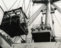 "Up and Away - Combat tents bound for Marines are lifted from #1 hold of S.S. Sir John Franklin to awaiting landing craft which shuttle the vital cargo to the piers within the city of Da Nang." A large wooden crate is lifted from the hold of a Navy ship onto the deck. Two sailors look on. It appears the crate is being lifted be a crane or some other machinery.