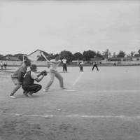 A group of American men are playing baseball - in the foreground one is swinging at a pitch.