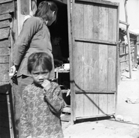 "Macau" Slum street scene. A young child looks at the camera with an adult standing behind her.