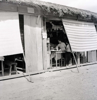 The outside of shop or restaurant. There are long awnings protecting the shop from the sun. There are two women inside.