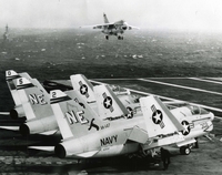 An A-7A Corsair II, the Navy's newest attack aircraft, comes in for a landing on the flight deck of the USS Ranger, with other A-7s being shown in the foreground.