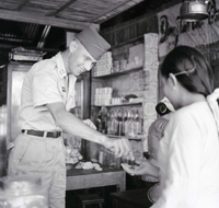 An American soldier hands some coins to a Vietnamese woman in a shop.