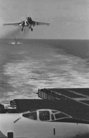 "7th Fleet" A view of the open ocean. A low-flying airplane approaches the aircaft carrier from which the photo was taken. In the background a second aircraft carrier can be seen.