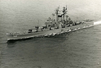 "The USS Newport News is shown cruising in the Tonkin Gulf. She is presently engaged in operations off North Vietnam immediately above the DMZ." A naval ship sails on the open water.