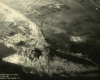 "Before and After near Thanh Hoa, North Vietnam - Navy jet pilots of Carrier Air Wing 15 pounded a railroad ferry complex northeast of Thanh Hoa Sep. 21-23, 1966. Targets included a thermal power plant, defending flak sites, railways, boxcars, and roads. After the raid shown in these before and after photos, Navy Intruder and Skyhawk pilots described the area as 'devastated.'" Aerial photo of a bombed landscape with roads, a village, a railway, a river, and farms.