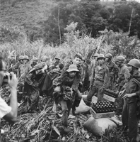 One Vietnamese soldier carries another on his back while other ARVN soldiers are seen in the background.