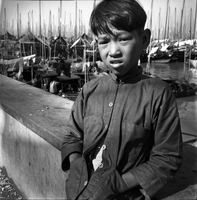 "Macau" A young boy standing in front of a marina of boats.