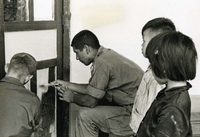 "Pleiku, Vietnam (Army IO) - Helping in the renovation of the sector girls' school here are (L to R) PFC Robert Harvey, Princeton, N.J. and PFC Amador Garcia, Los Angeles. Both are members of the Army's 173rd Airborne Brigade. The school has been closed for several months because of damages incurred during its emergency use as refugee and troop quarters." Two American soldiers paint a door while two Vietnamese children look on.