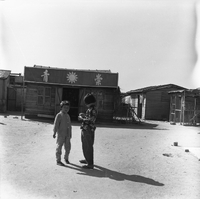 "Macau" Two young children standing in front of some wooden buildings.