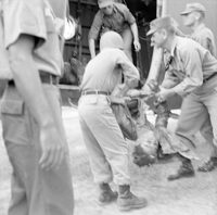 "AP WIA/KIA Dead/Dying", a group of soldier carrying an injuried person into a house(?), hospital(?)