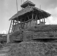 "Ashau II", a grass house from lower view with a men standing in front of it